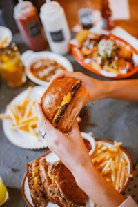 person holding burger with some of the best burger sides in background including fries, chili, etc